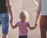 Rodzina idzie razem, trzymając się za ręce. Dziecko z blond włosami, w kolorowej bluzce, między rodzicami. Może to być obraz rodziny, która radzi sobie z zaburzeniami zachowania ICD 10.