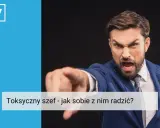 Wściekły mężczyzna w garniturze wskazuje palcem, ukazując cechy toksycznego szefa.