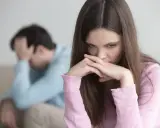 Zmartwiona kobieta z dłońmi przy ustach, obok mężczyzna z ręką na głowie. W tle widać kanapę. Obraz symbolizuje **relationship ocd**.
