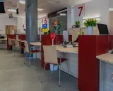 Puste biurka z krzesłami w urzędzie, gdzie przestrzegana jest proksemika. Widać numery stanowisk i tabliczki informacyjne.