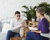 Mężczyzna w okularach rozmawia z kobietą, która notuje. Wyglądają jak na sesji z coachem psychologiem.