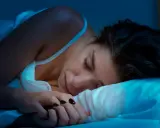 Kobieta śpi, ale budzik sugeruje, że to może być kolejna noc bez snu. Co to insomnia?