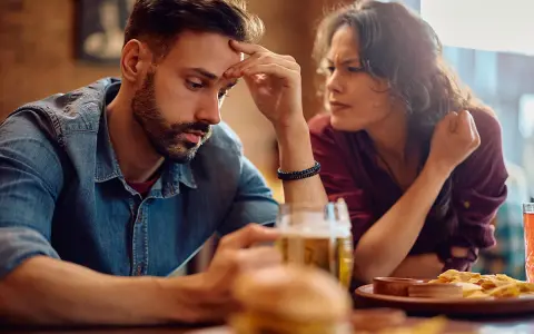 Mężczyzna z wycofaniem emocjonalnym opiera czoło na dłoni, podczas gdy kobieta patrzy na niego z frustracją.