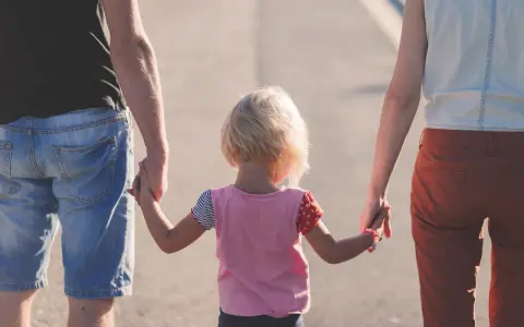 Rodzina idzie razem, trzymając się za ręce. Dziecko z blond włosami, w kolorowej bluzce, między rodzicami. Może to być obraz rodziny, która radzi sobie z zaburzeniami zachowania ICD 10.