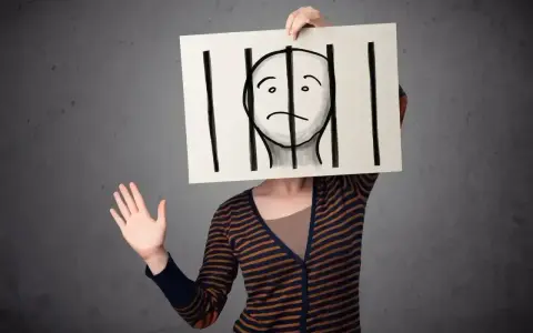 Osoba trzyma tabliczkę z rysunkiem twarzy za kratami. Czy to paranoik, który czuje się uwięziony?