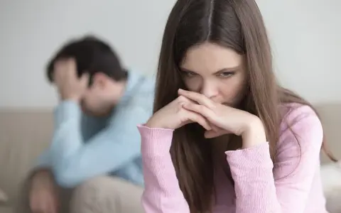 Zmartwiona kobieta z dłońmi przy ustach, obok mężczyzna z ręką na głowie. W tle widać kanapę. Obraz symbolizuje **relationship ocd**.