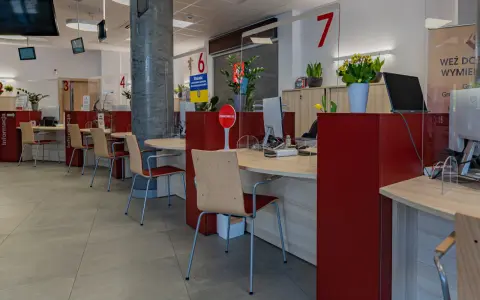 Puste biurka z krzesłami w urzędzie, gdzie przestrzegana jest proksemika. Widać numery stanowisk i tabliczki informacyjne.