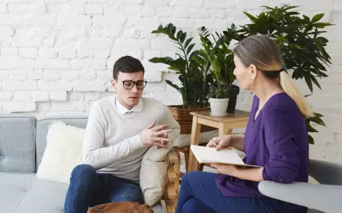 Mężczyzna w okularach rozmawia z kobietą, która notuje. Wyglądają jak na sesji z coachem psychologiem.