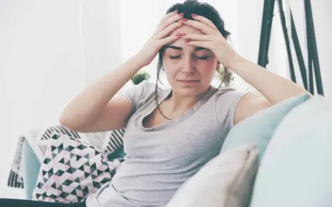 Kobieta z rękami na skroniach, cierpiąca na ból głowy. Czy to psychosomatyka, co to znaczy?