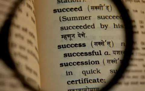Słownik pod lupą ukazuje definicję słowa "success", czyli sukces. To droga do osiągnięcia celu.