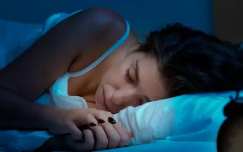 Kobieta śpi, ale budzik sugeruje, że to może być kolejna noc bez snu. Co to insomnia?