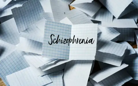 Rozrzucone kartki w kratkę, na jednej napis "Schizophrenia". Obraz symbolizuje chaos myśli, objawy schizofrenii hebefrenicznej.