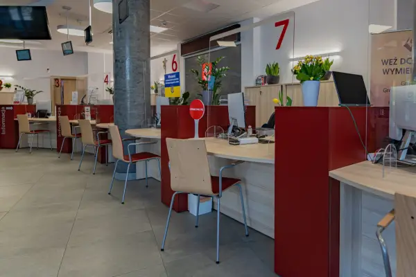 Puste biurka z krzesłami w urzędzie, gdzie przestrzegana jest proksemika. Widać numery stanowisk i tabliczki informacyjne.